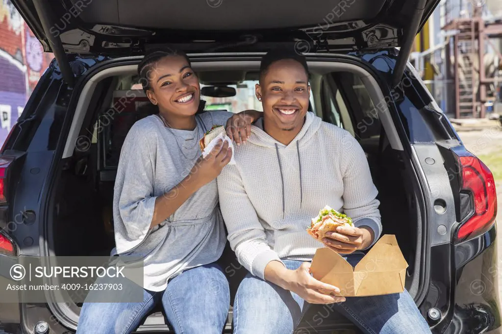 Portrait of young African American couple having impromptu picnic lunch in the back of their vehicle.