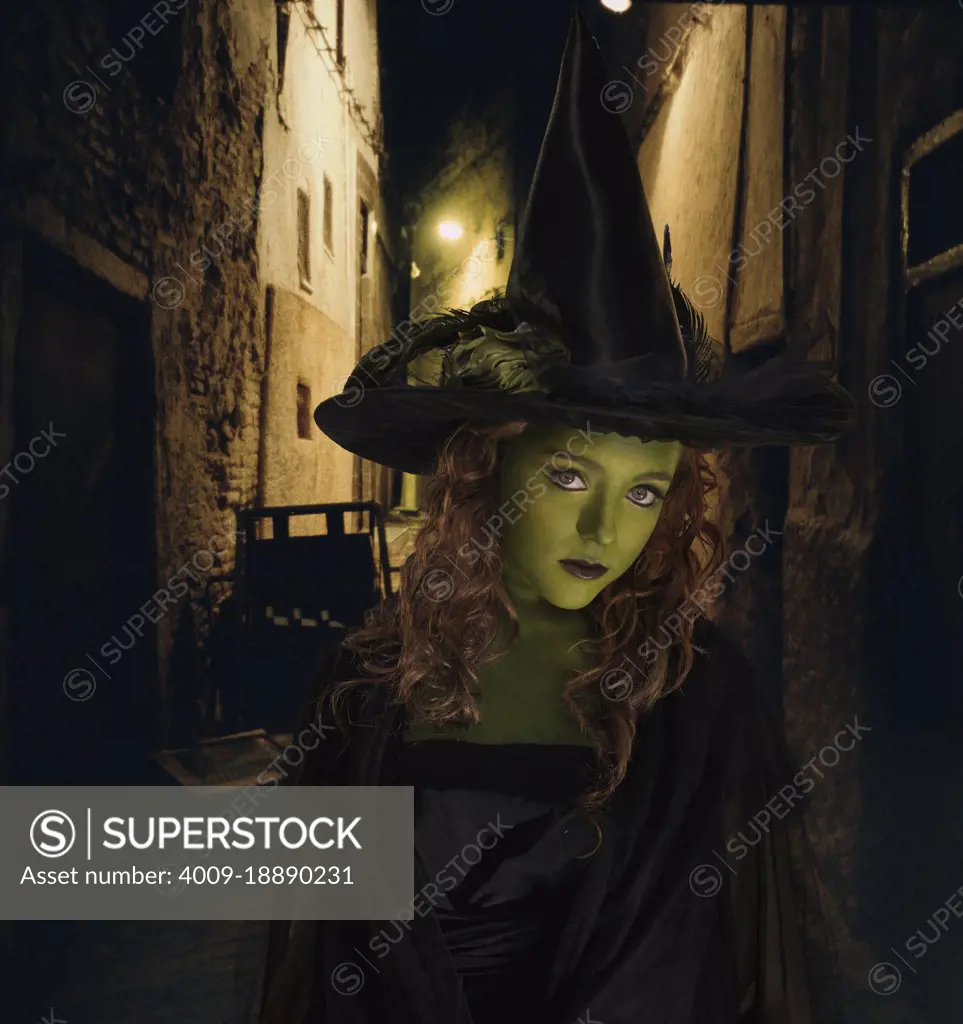 Young girl dressed as witch standing in front dark alley 