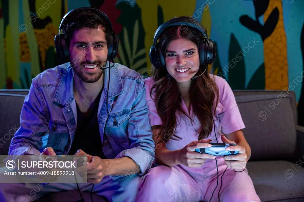 Excited friends playing video game together at home wearing microphone headsets.