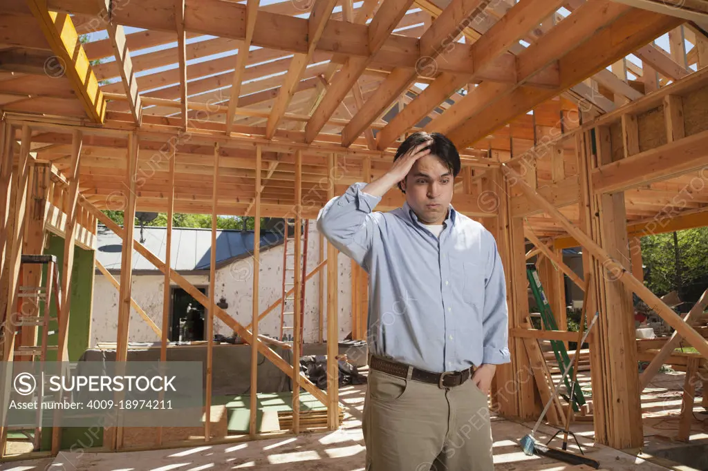 Man hand on his head looking down in worry at a residential construction site