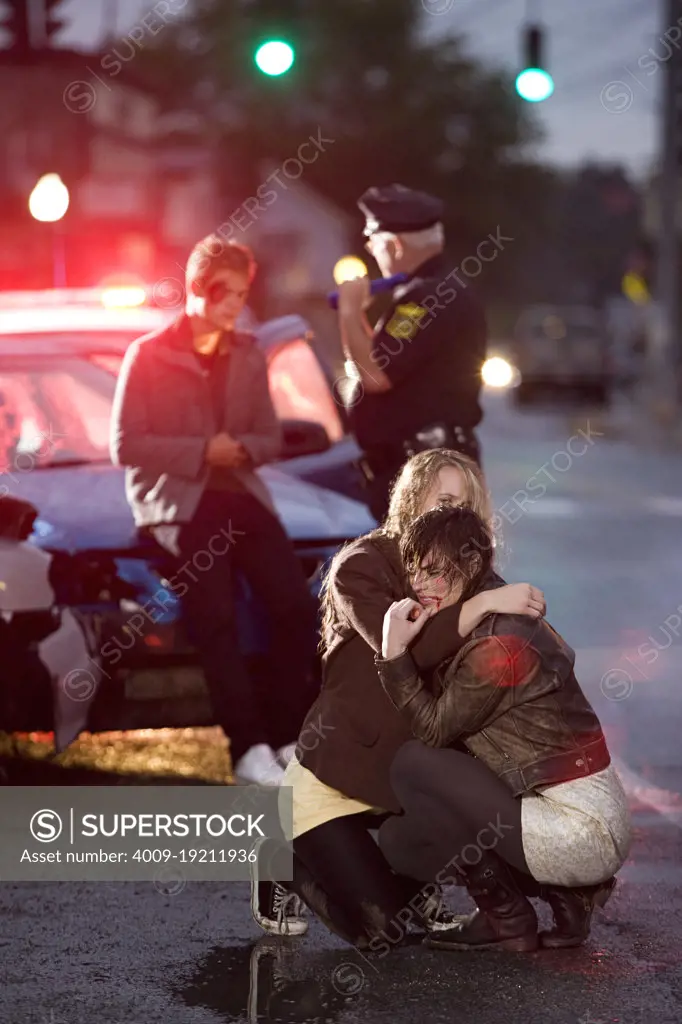 Injured young women on the sceen of an automobile accident , police officer talking with young man in background 