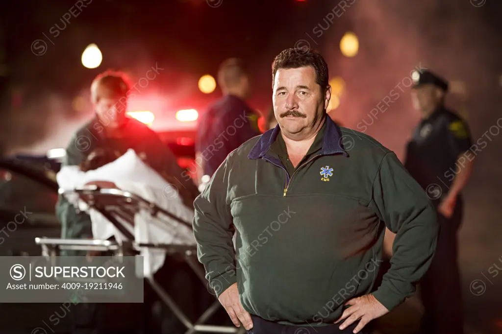 Portrait of EMT, with Paramedic helping injured people on scene of automobile accident and police talking in background  