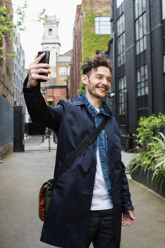 Portrait of young man in alley holding cell phone taking a selfie