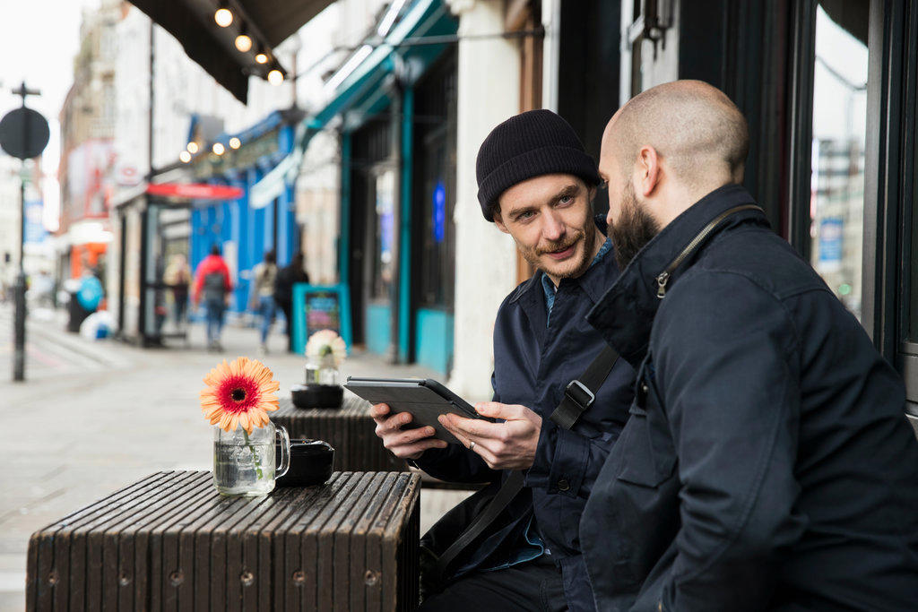Two men sitting at outdoor cafe table looking at tablet