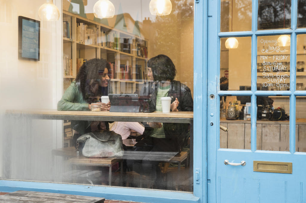 Two women sitting in window of cafe looking at tablet