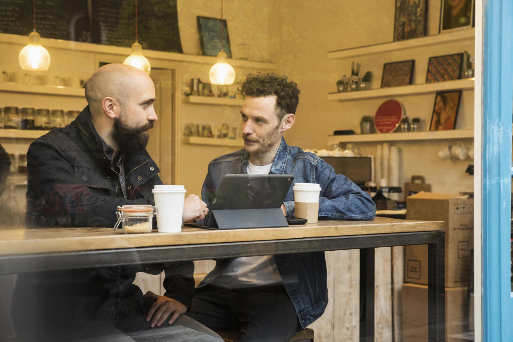 Friends sitting in window of cafe with tablet