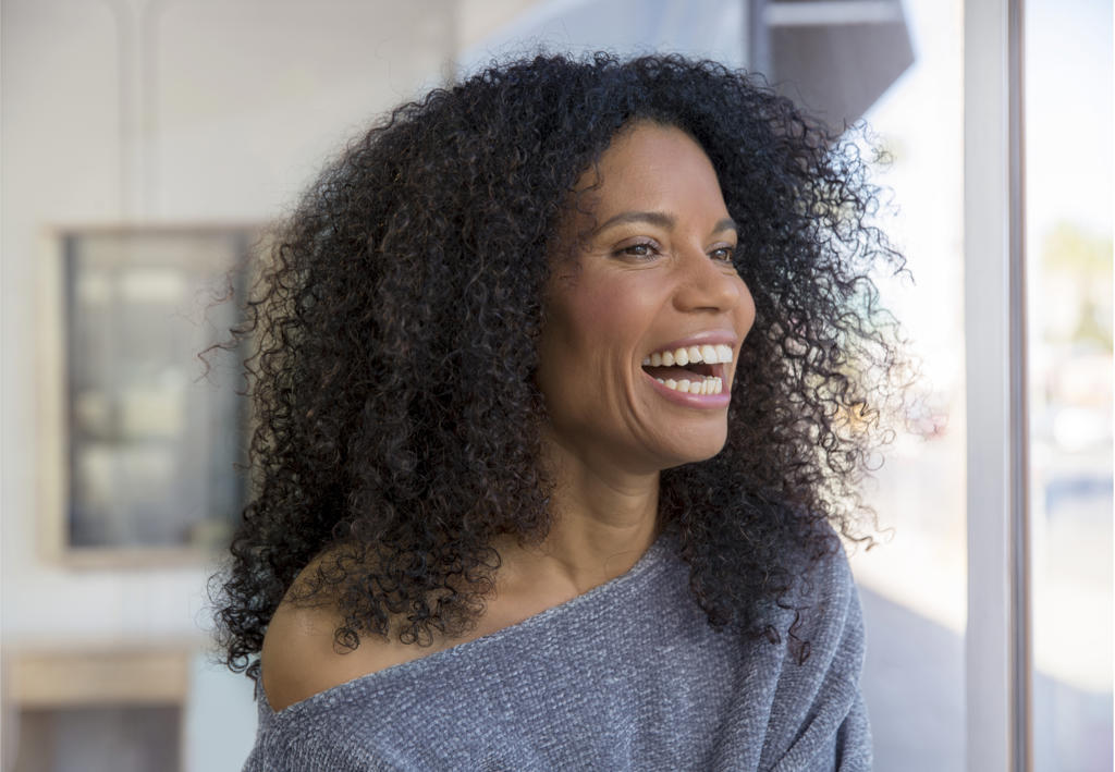 Mixed race, middle-aged woman laughing and looking out the window.