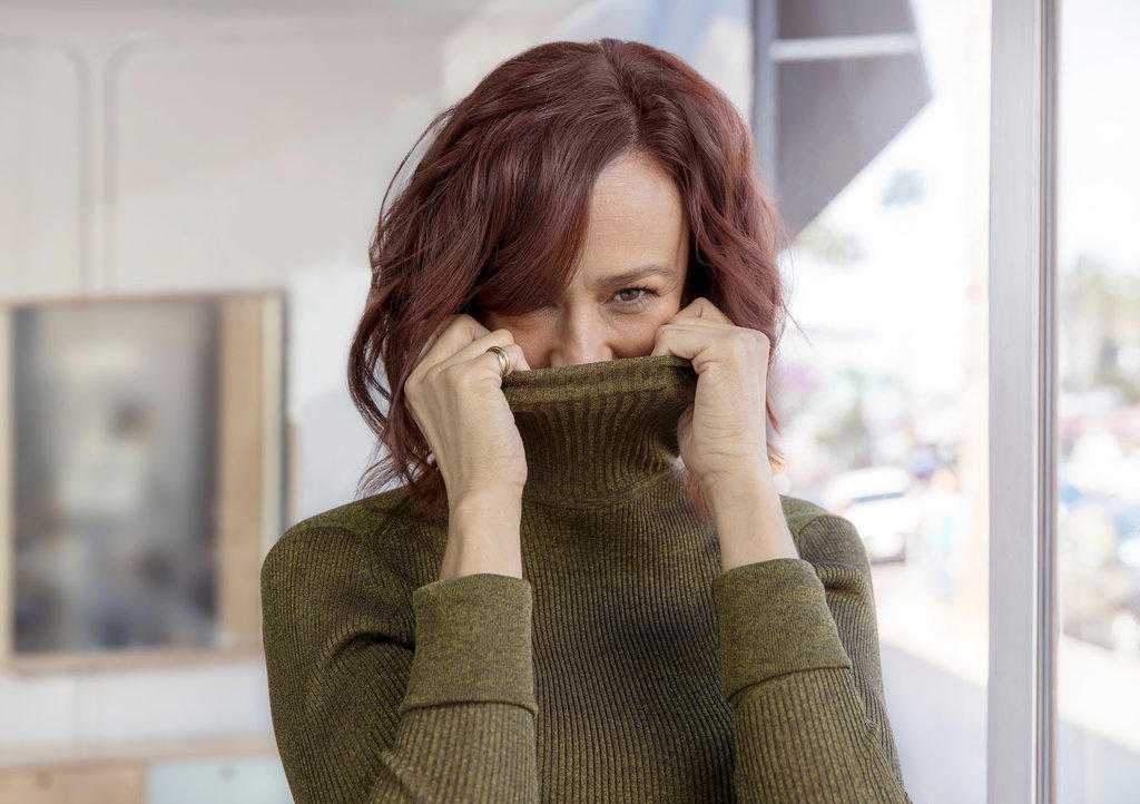 A playful middle-aged woman hides her face in her turtleneck sweater.