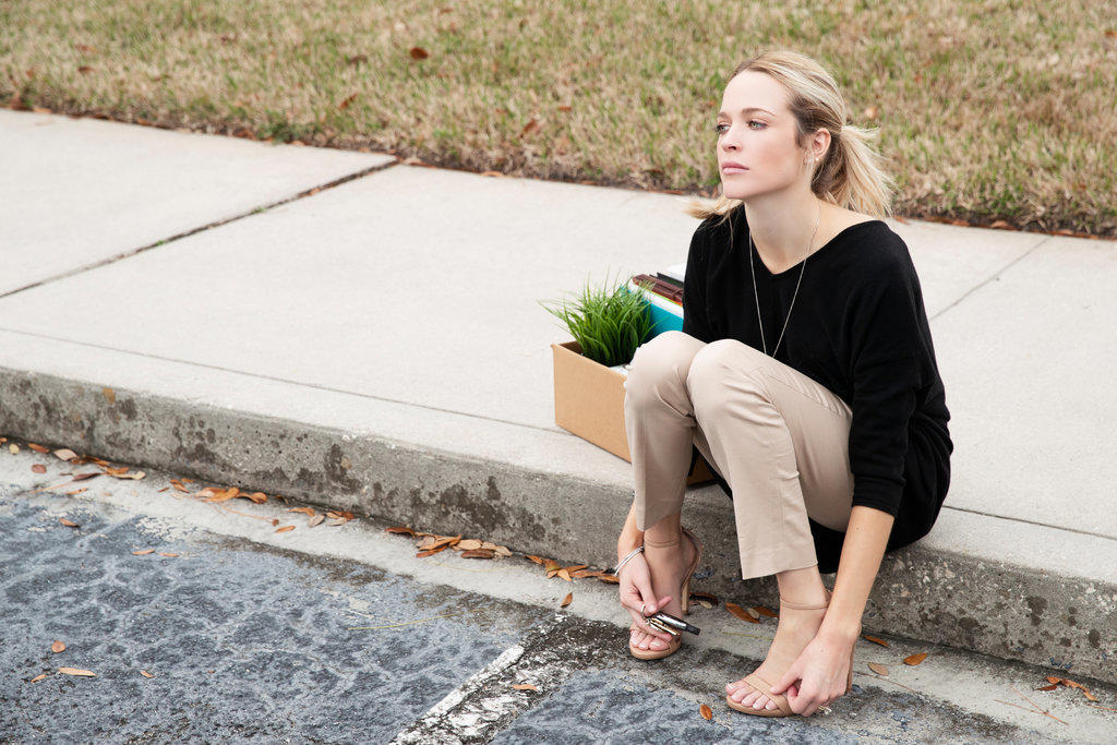 Distraught employee sitting on the curb with a box of her belongings