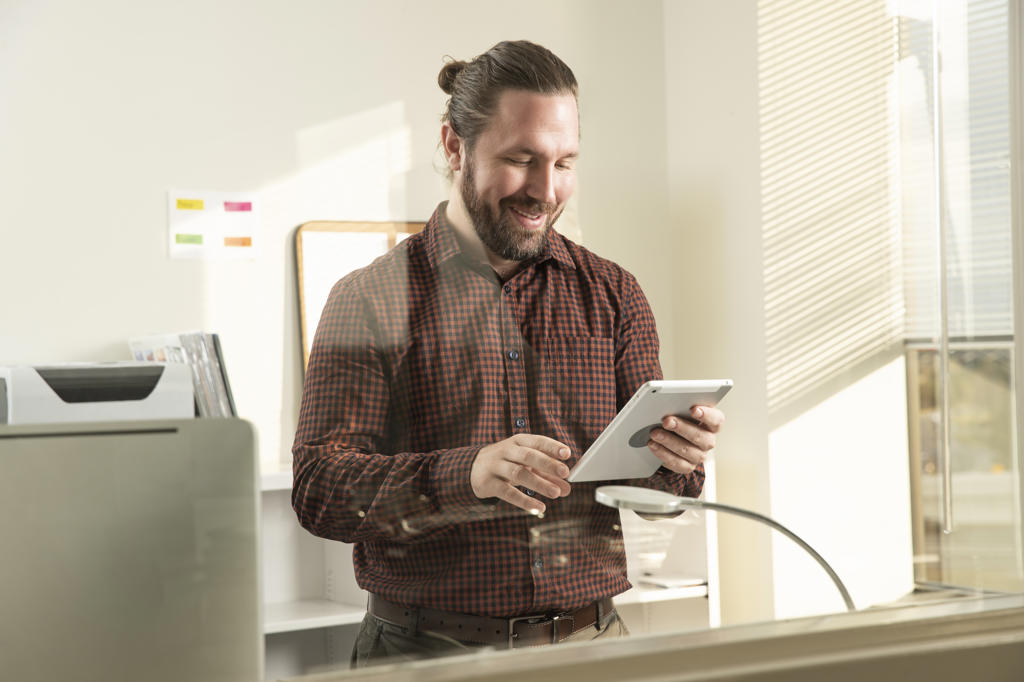 A man standing in his office looking at a tablet.