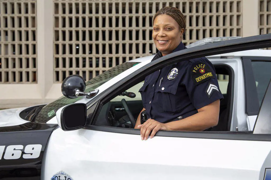 Policewoman standing in door of Police car looking towards camera smiling 