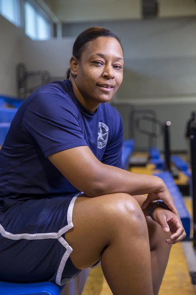 Portrait of Police woman sitting on bleachers in gymnasium looking towards camera smiling 