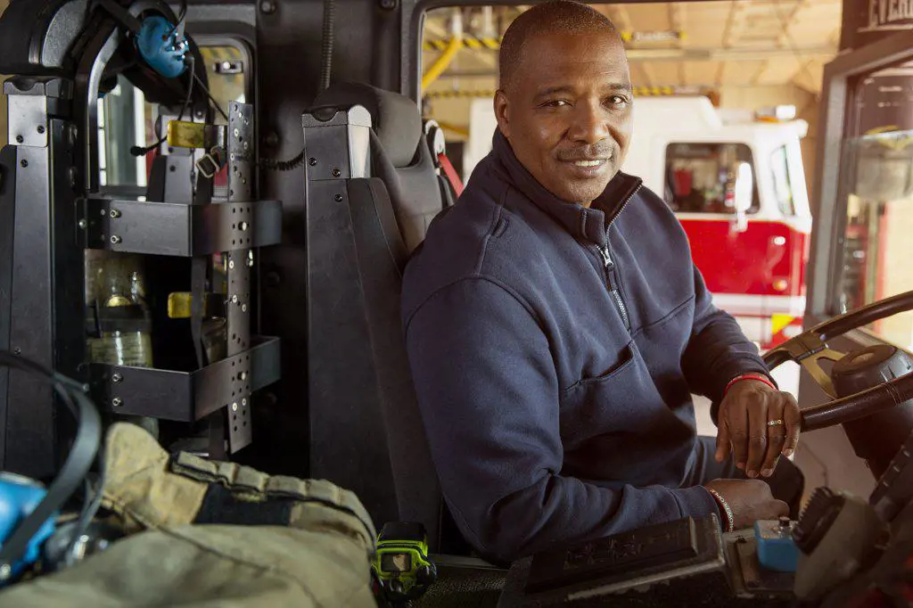 Portrait of Fireman Sitting in Drivers seat of firetruck looking towards camera  smiling 