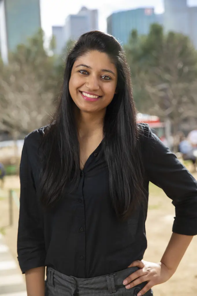 Smiling portrait of young ethnic woman with long black hair standing in park wearing black blouse
