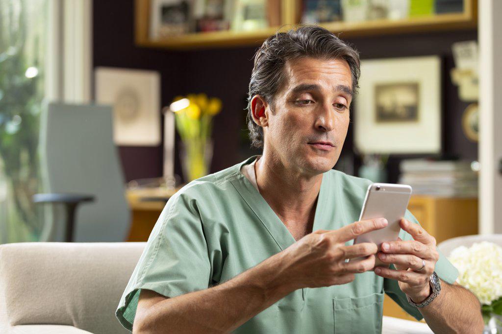 Hispanic Male doctor practicing tele-medicine from his home office, Talking to patient via video call on cell phone