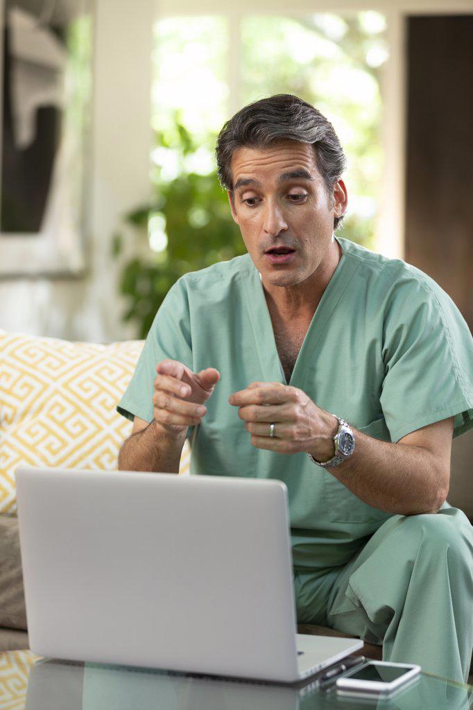 Hispanic Male doctor practicing tele-medicine from his home using laptop computer to consult patient on video call 