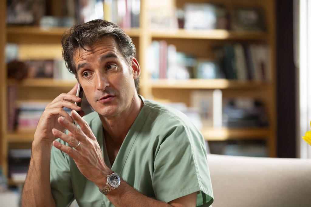 Hispanic Male doctor practicing tele-medicine from his home office, Talking to patient on cell phone 
