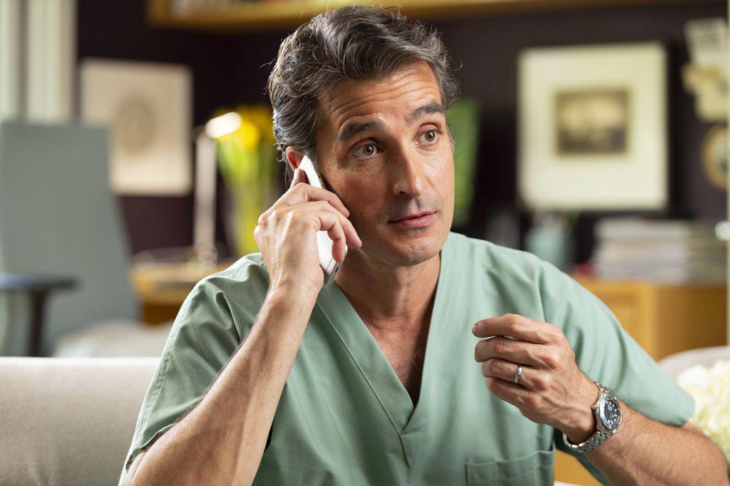 Hispanic Male doctor practicing tele-medicine from his home office, Talking to patient on cell phone