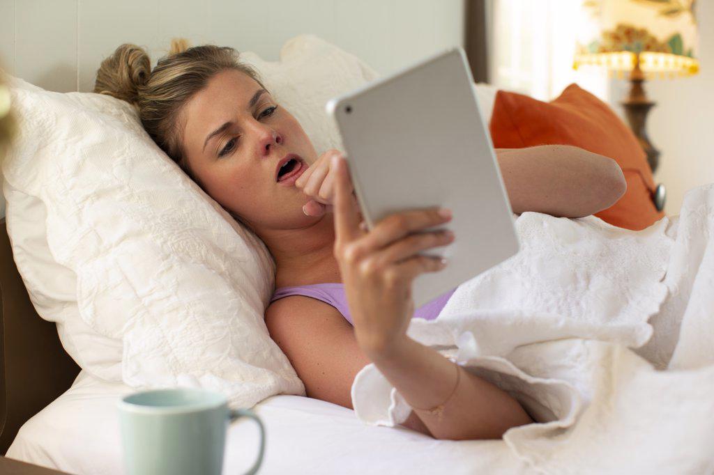 Coughing young woman in her bed with using tablet to check in with doctor 
