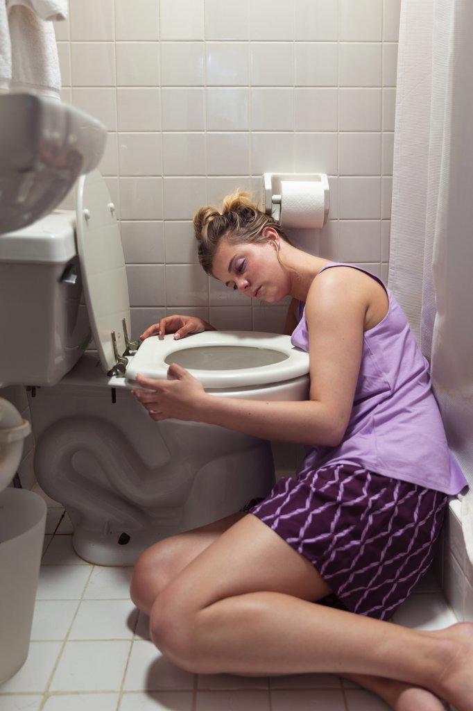 Young woman on the floor in her bathroom feeling sick next to toilet