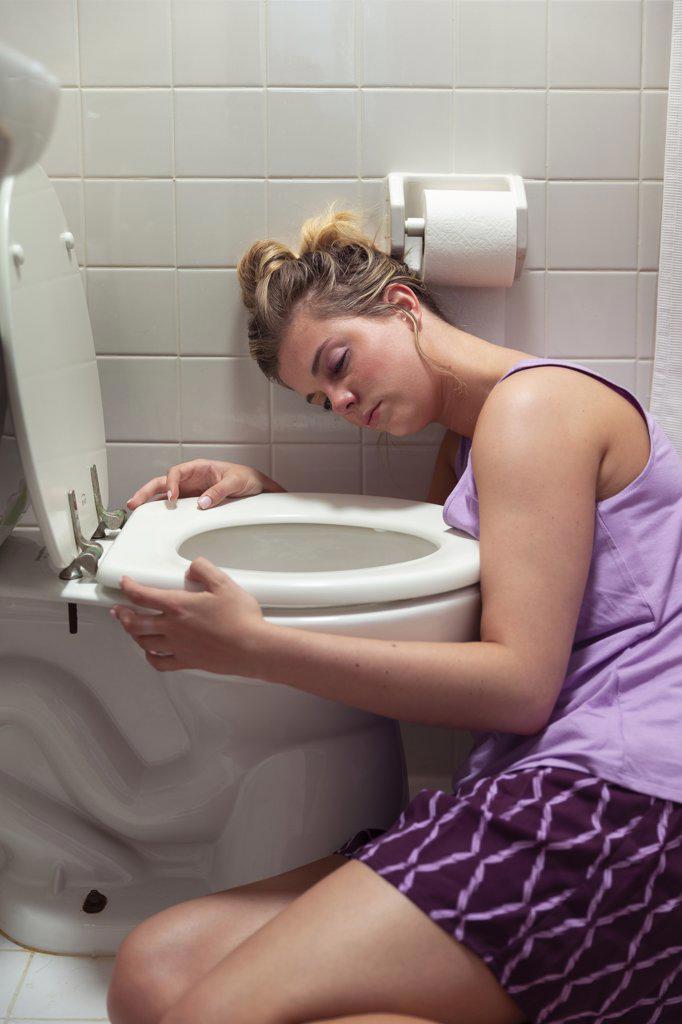 Young woman on the floor in her bathroom feeling sick next to toilet