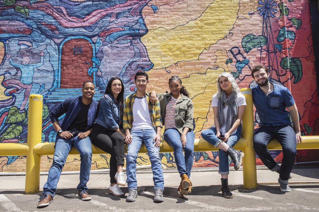 Group portrait of young co-workers hanging out in front of graffitied wall 