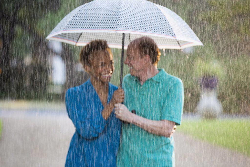 Older couple walking through park with umbrella in the rain, out of focus 