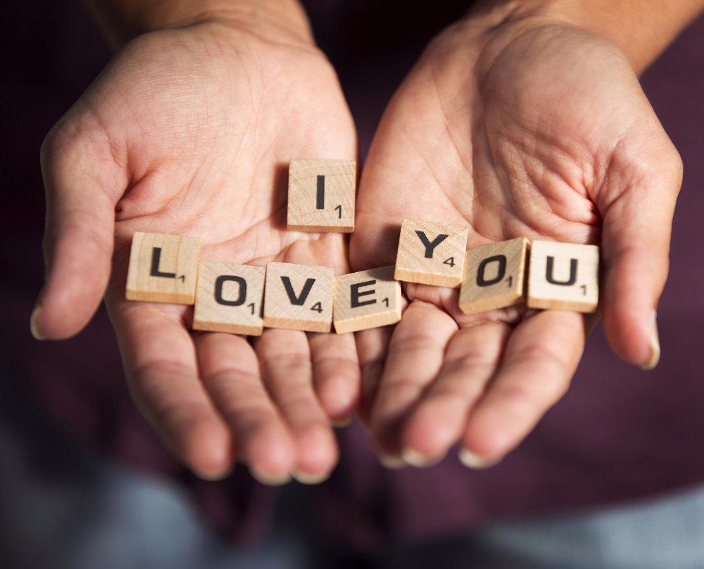 Detail shot of woman holding loose scrabble pieces with the  phrase “I Love You” spelled out on the little wooden blocks. Love