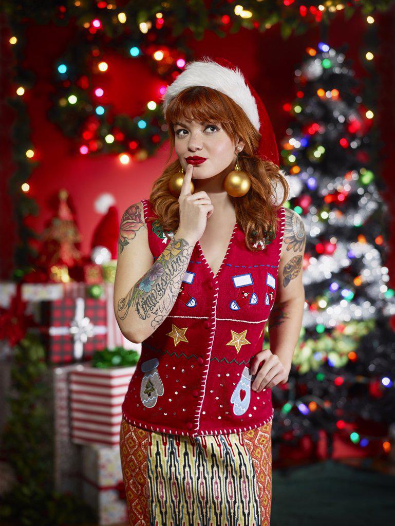 Portrait of red headed woman with tattoos in ugly Christmas sweater/vest making a provocative face