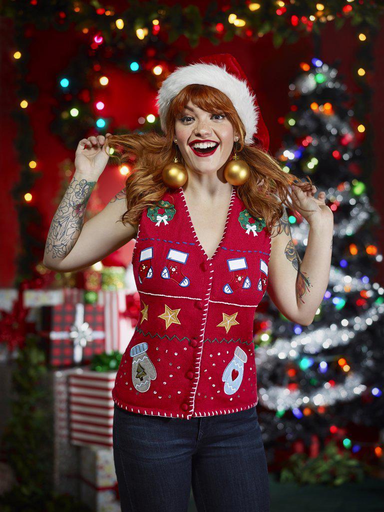 Portrait of red-headed woman with tattoos in an "ugly" Christmas vest making a face and plying with her hair