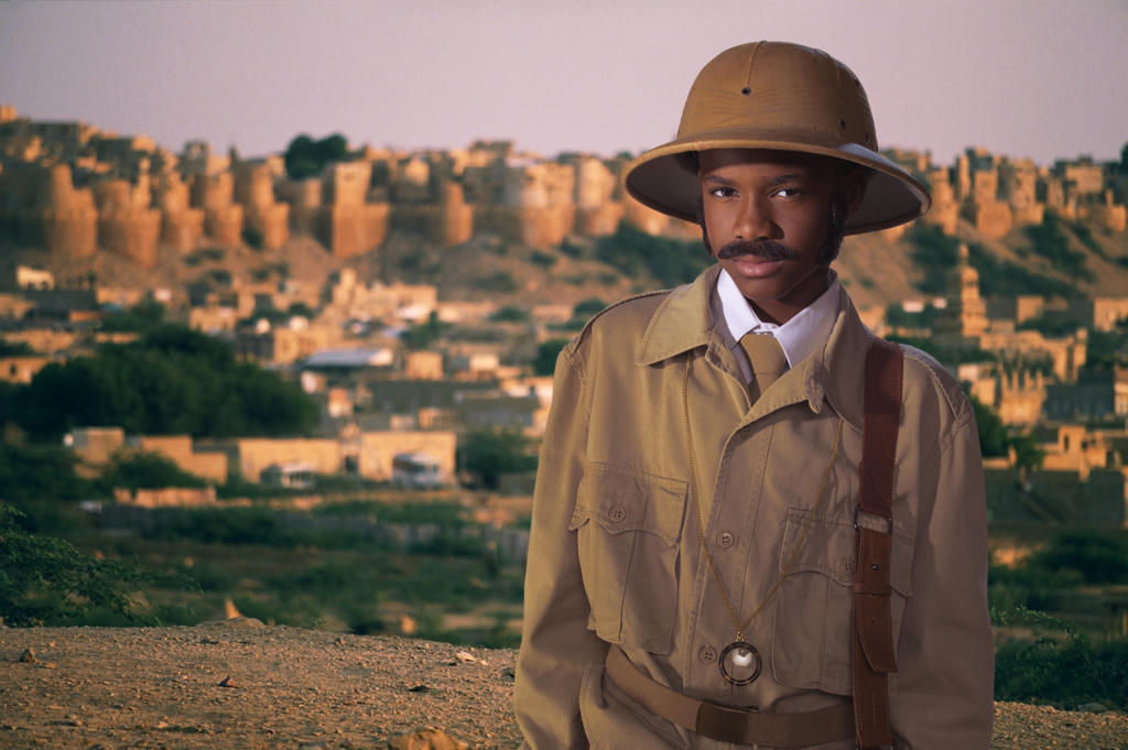 Young boy dressed as Archaeological Egyptologist standing in front of village out of focus in background 