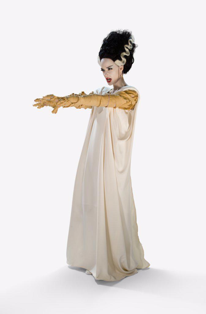 Woman dressed as the Bride Of Frankenstein Halloween costume, holding her arms out looking off camera, against a white background
