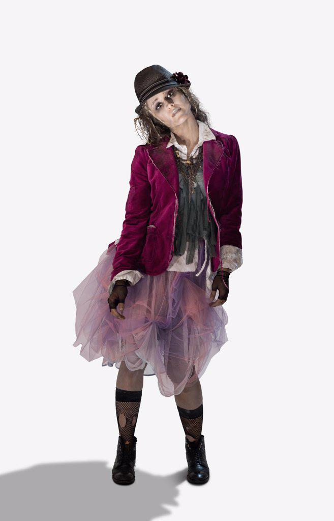 Woman dressed up as a zombie wearing a fedora and ripped stocking looking into camera with dead expression for Halloween, on white background