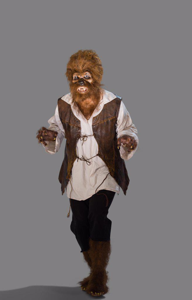 Full length portrait of a person dressed up in a Wolfman costume for Halloween making a evil face at camera, against white background