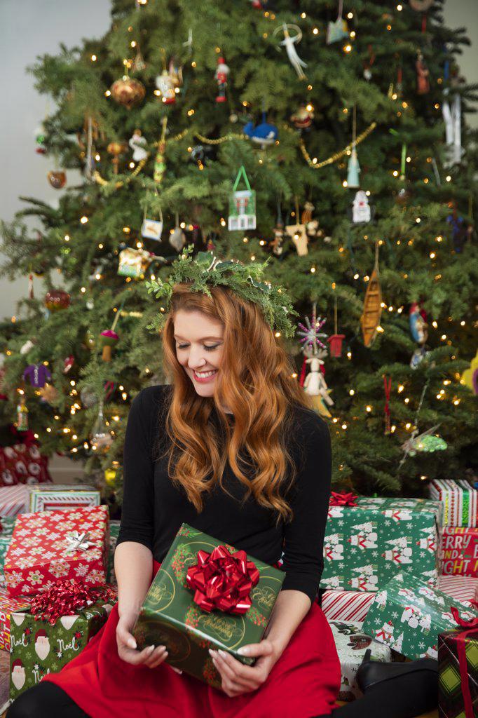 Portrait of a young redheaded woman holding a Christmas present sitting in from of lit tree.