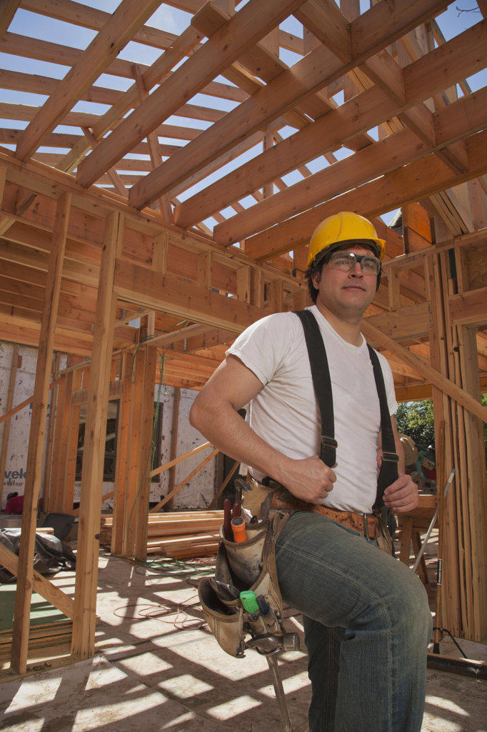 Portrait of a man wearing a hard hat and a tool belt while standing on the construction site