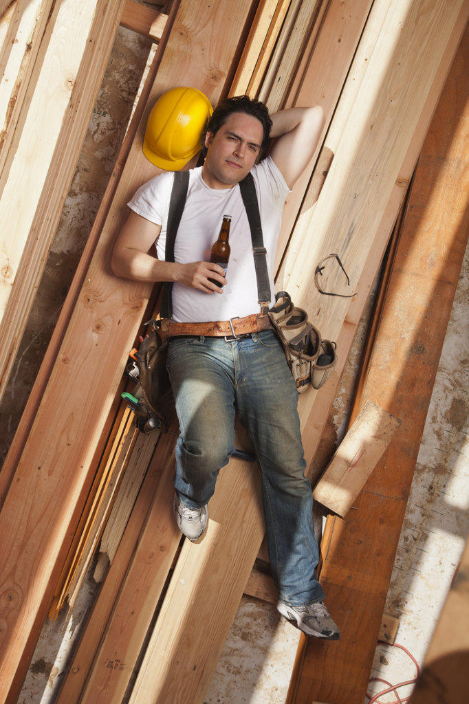 Aerial view of a man drinking a beer while resting on planks of wood at a residential construction site