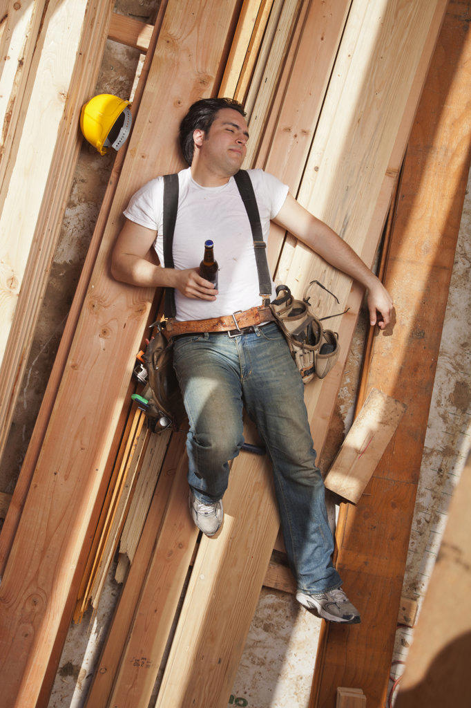 Aerial view of a man drinking a beer while resting on planks of wood at a residential construction site