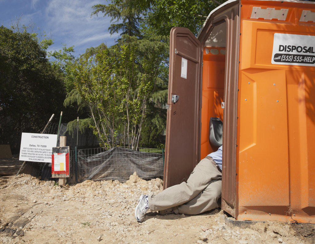 Man lying half inside and half outside of a portable toilet at a residential construction site