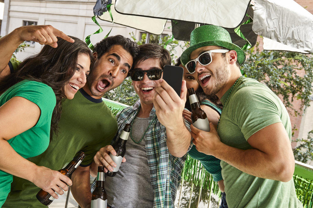 Group of friends hanging out on balcony taking a selfie and drinking beer celebrating St. Patrick's Dat.