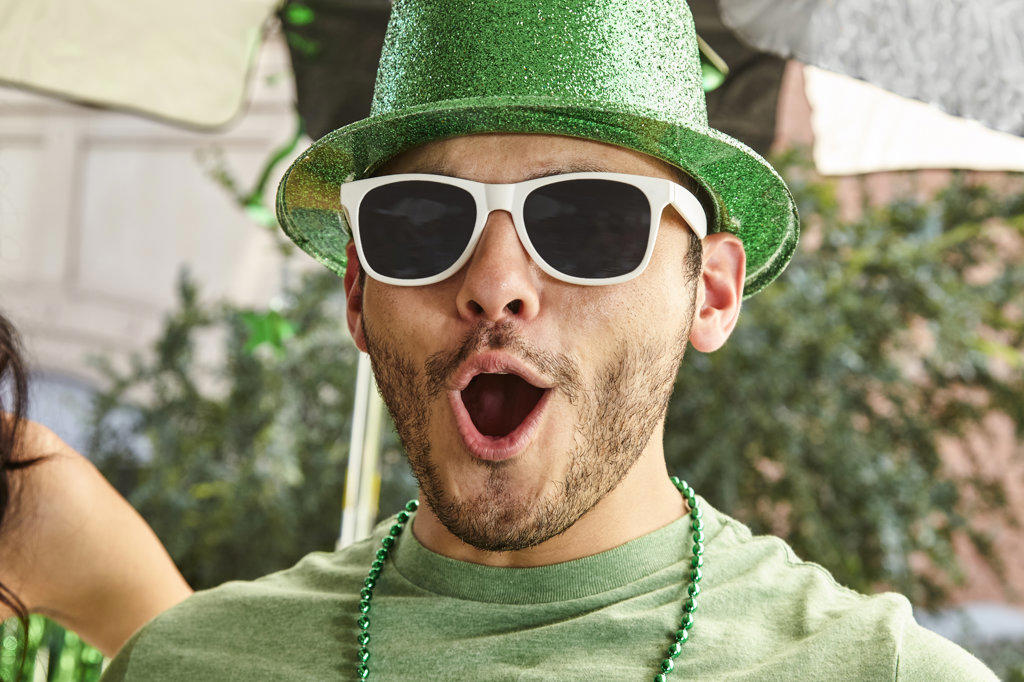 Happy St. Patrick's Day man in a green hat and sunglasses screaming in celebration while at party
