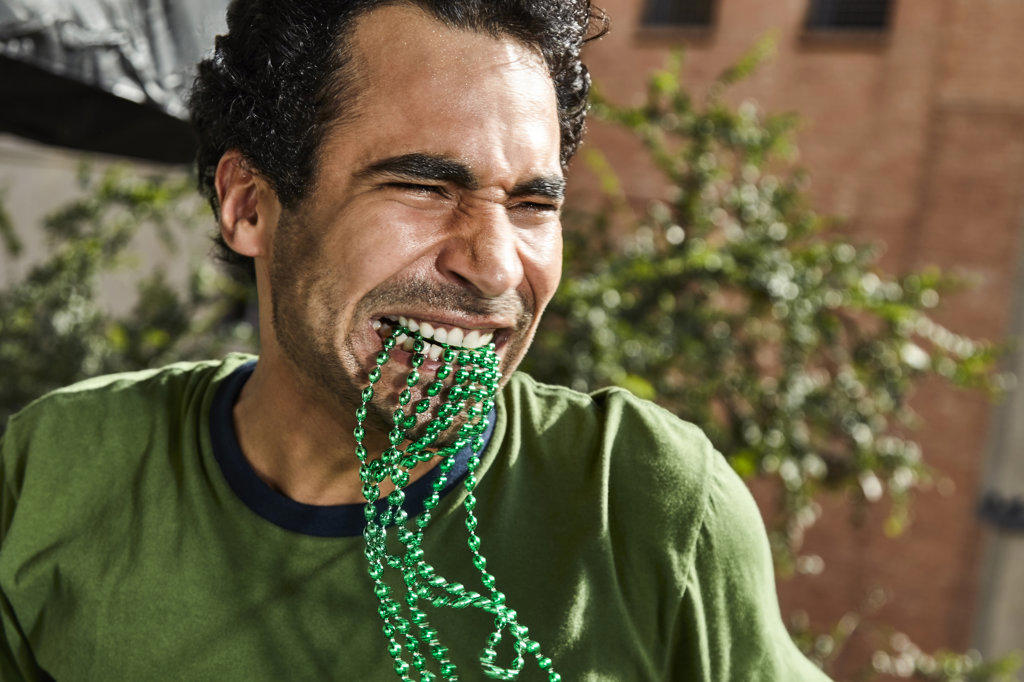 Happy man with green St Patrick's Day beads in his mouth dancing at a party.