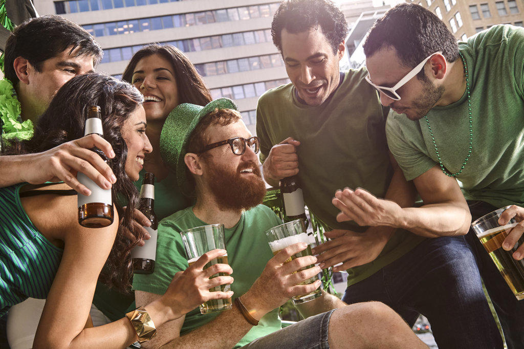 Group of friends hanging out on balcony of bar enjoying the St Patrick's Day festivities drinking beer.
