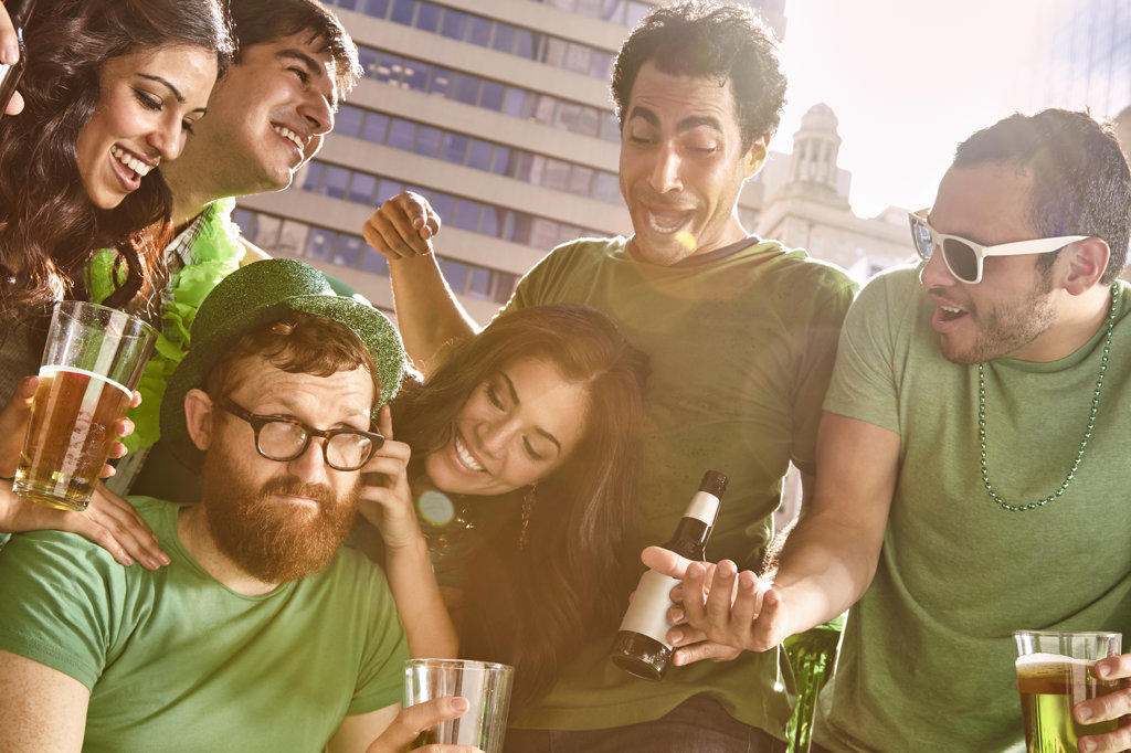 Group of friends gathered around one man who is refusing to have fun at St Patrick's Day party