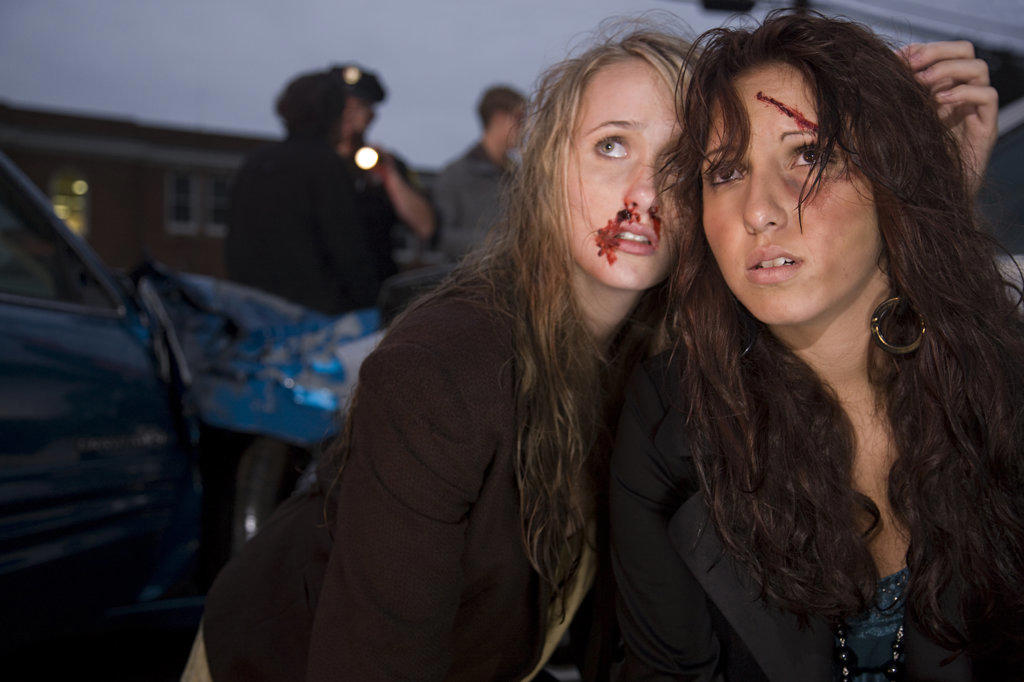 Injured young women sitting in street  with scene of an automobile accident behind them