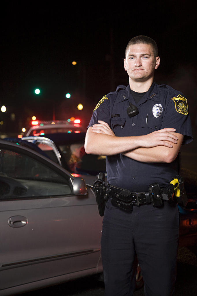 Portrait of Police officer on scene of automobile accident standing in front of wreck with arms crossed 
