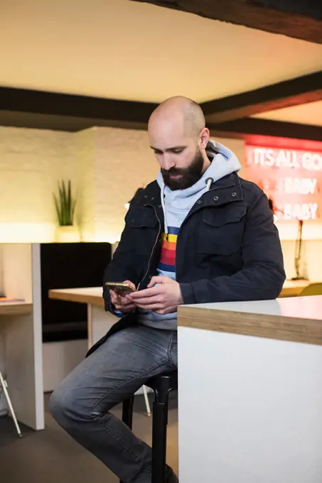 Man checking his phone while sitting at table in co-working space