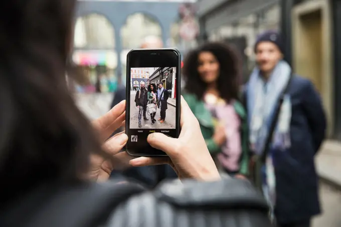 Woman on the streets of London taking  photo of friends with mobile phone
