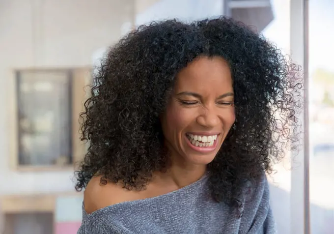 Mixed race, middle-aged woman laughing in a brightly lit room.