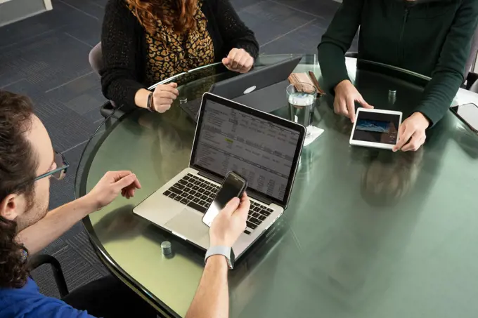 Overhead shot of three people on laptops and tablets during a meeting.